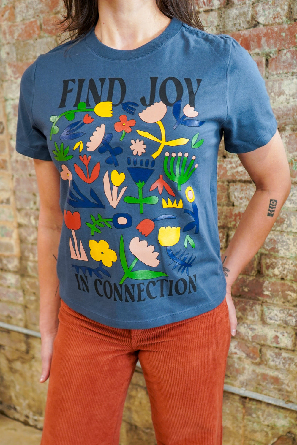 Person wearing a blue t-shirt with colorful graphics and text against a brick wall.