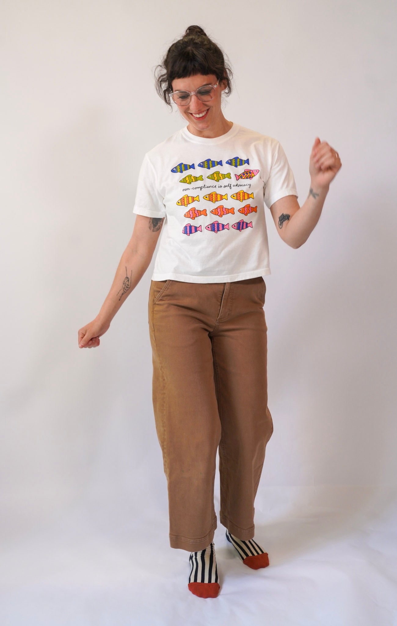 Person wearing a white t-shirt with colorful fish design and brown pants on a white background