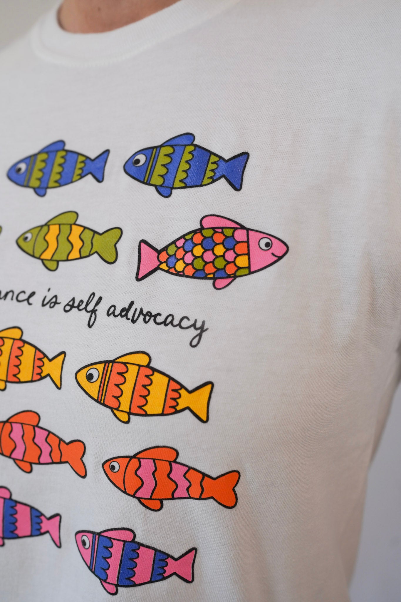 White t-shirt with colorful fish illustrations and text on a plain background