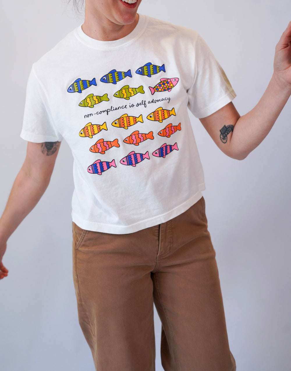 Person wearing a white t-shirt with colorful fish graphics and text on a plain background