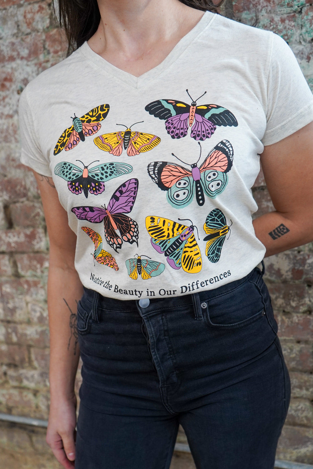Person wearing a white t-shirt with colorful butterfly designs against a brick wall.