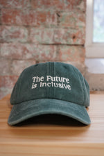 Green cap with 'The Future is Inclusive' text on a wooden surface.
