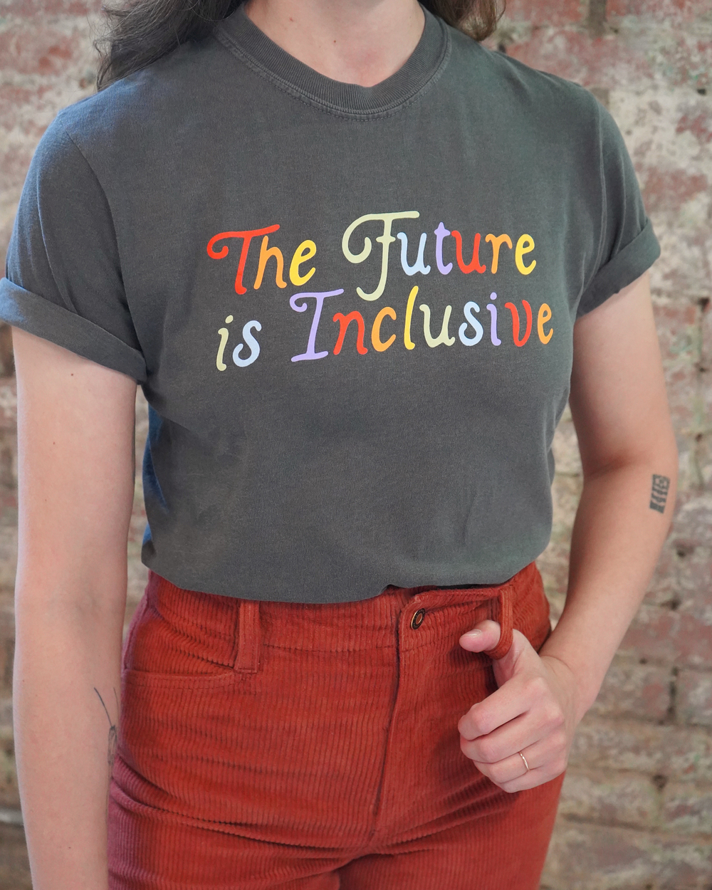 Person wearing a t-shirt with 'The Future is Inclusive' in colorful letters against a brick wall.
