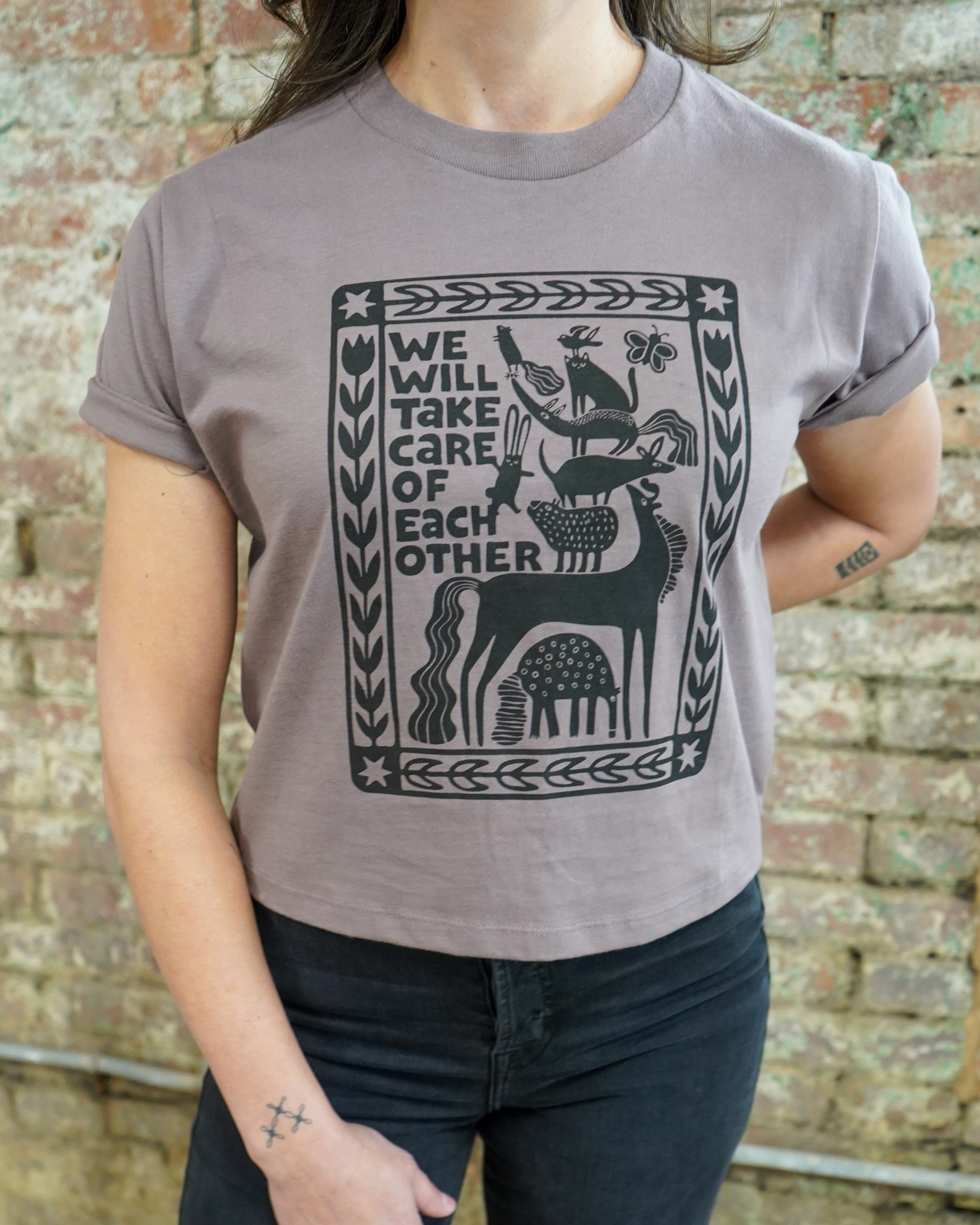 Person wearing a gray t-shirt with a black graphic design and text against a brick wall.