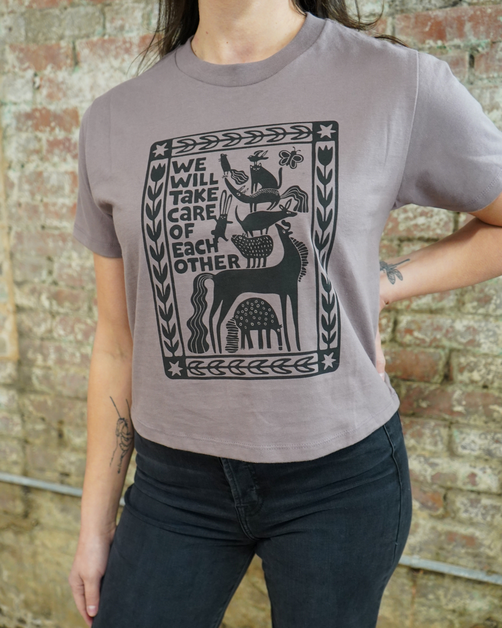 Person wearing a gray t-shirt with a graphic design and text against a brick wall.