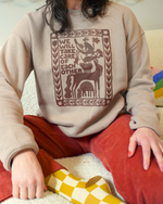 Person wearing a beige sweatshirt with a graphic design and text, sitting on a colorful rug.