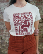 Person wearing a white t-shirt with a red graphic design and text against a brick wall.