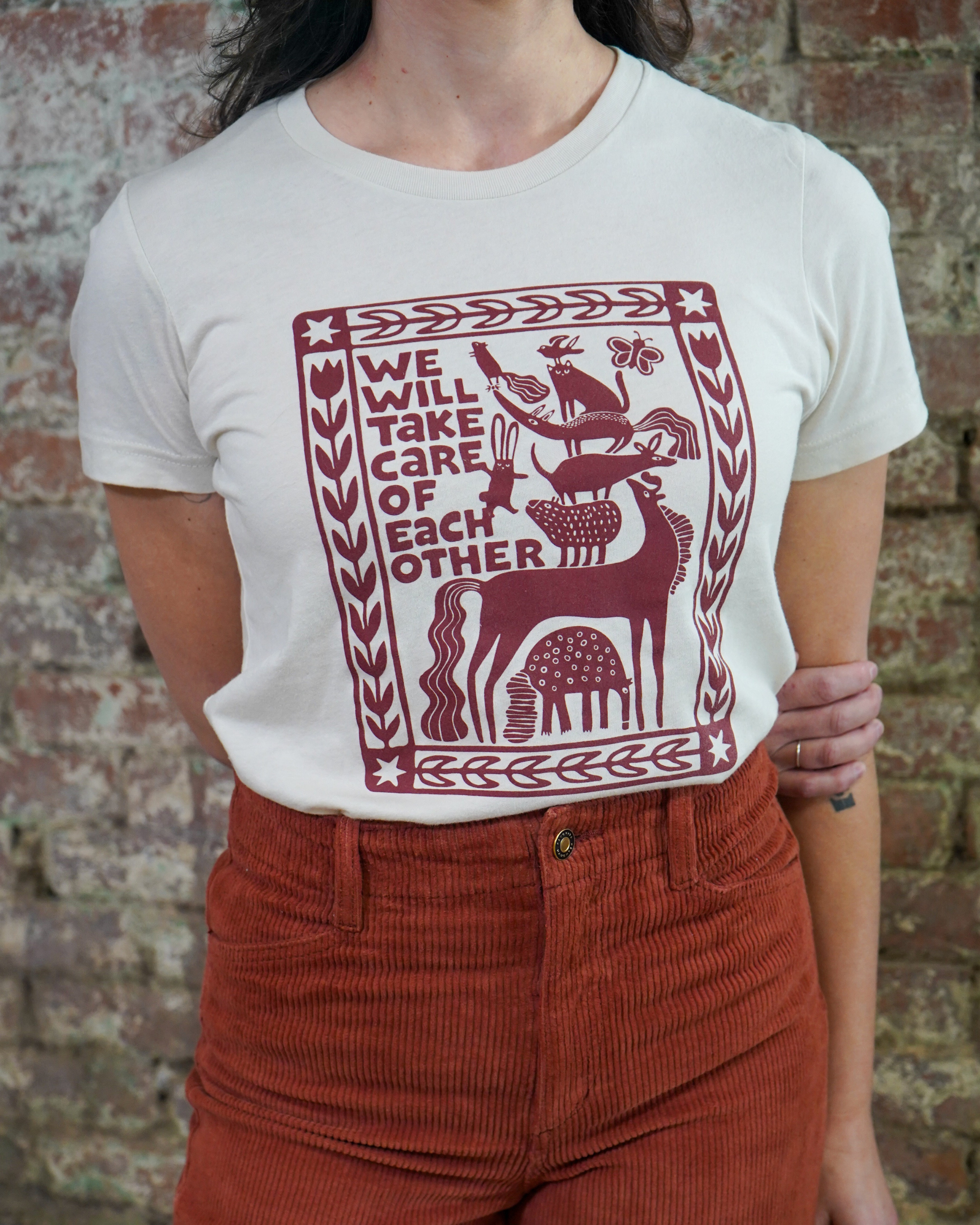 Person wearing a white t-shirt with a red graphic design and text against a brick wall.