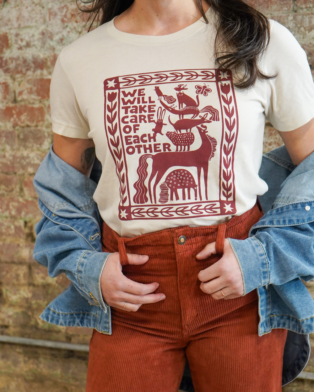 Person wearing a white t-shirt with a red graphic design and text, paired with a denim jacket and corduroy pants.