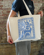 Person holding a tote bag with blue graphic design against a brick wall.