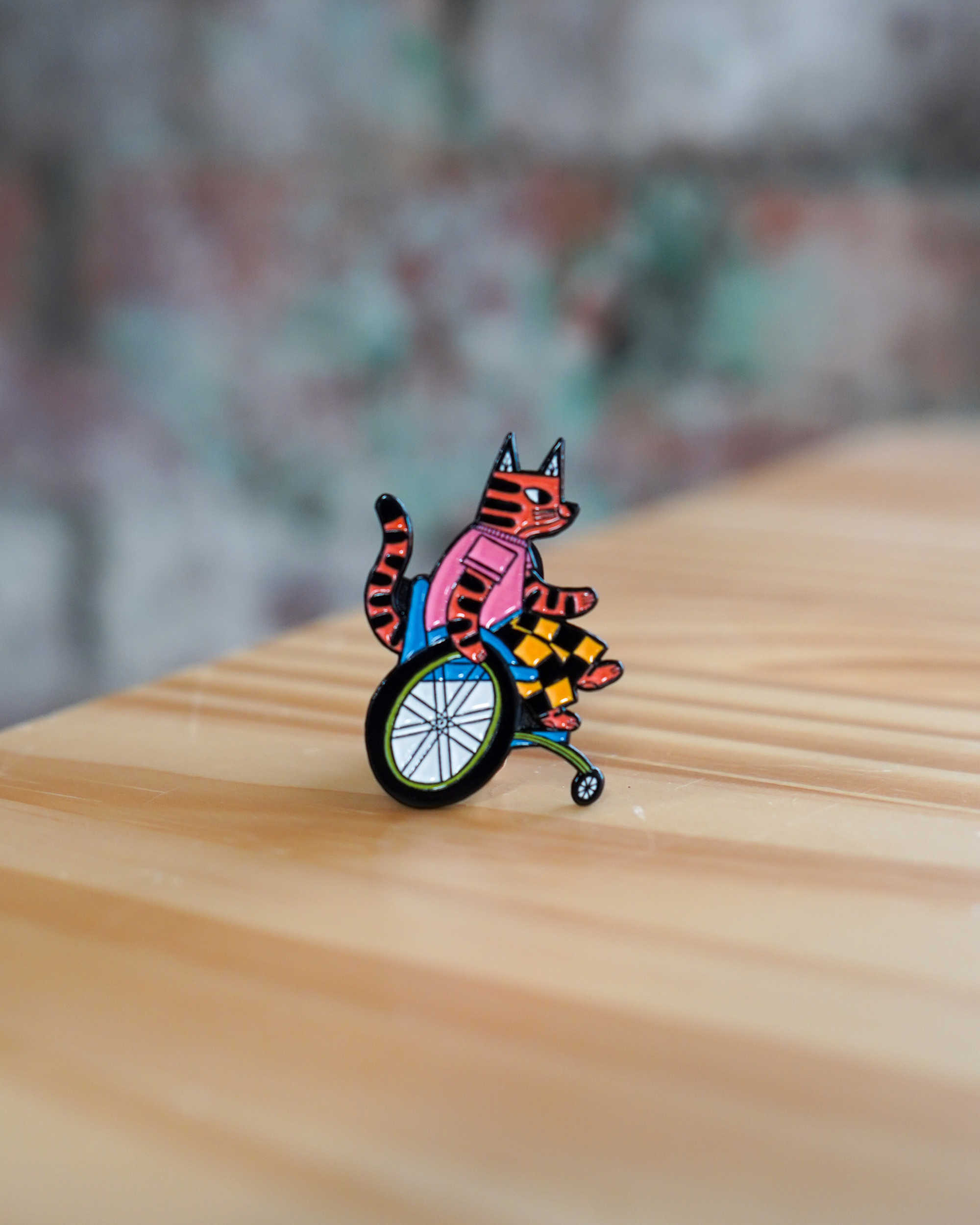 Colorful cat in a wheelchair pin on a wooden surface with a blurred background